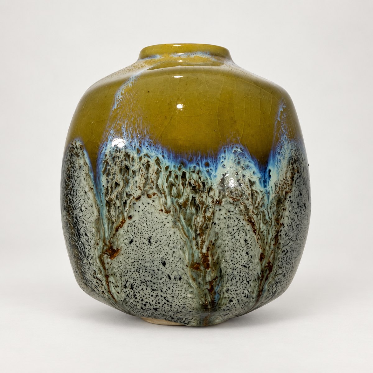 Slipcast form, ochre-olive shoulder breaking blue over a speckled grey base with iron drips